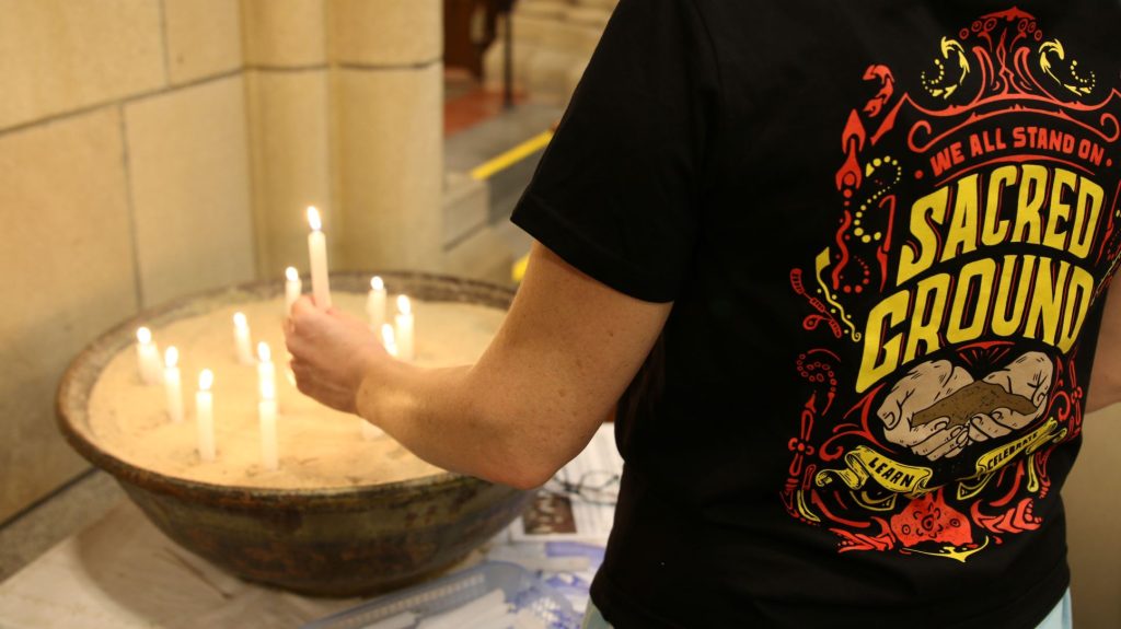 a Wiradjuri Cathedral community member wearing a “We all stand on sacred ground” t-shirt while lighting a candle 