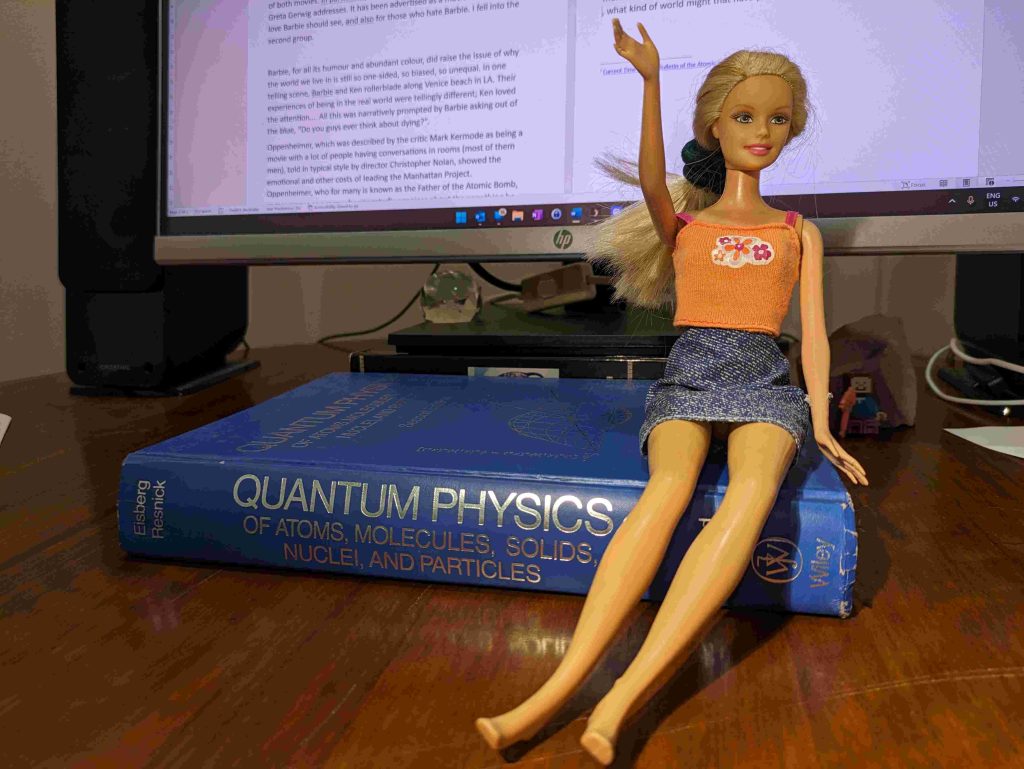 Image of a Barbie doll sitting on a physics book, representing "Barbenheimer"